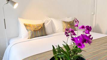 Habitación de hotel con cama, almohadas, lámpara y una orquídea en maceta.