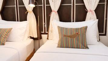 Habitación de hotel con dos camas, ropa de cama blanca, almohadas a rayas y cortinas atadas con cintas.