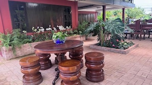 An outdoor seating area with a round wooden table and matching stools, surrounded by potted plants and a brick wall. - Retro at Mae Rim (Mae Rim)