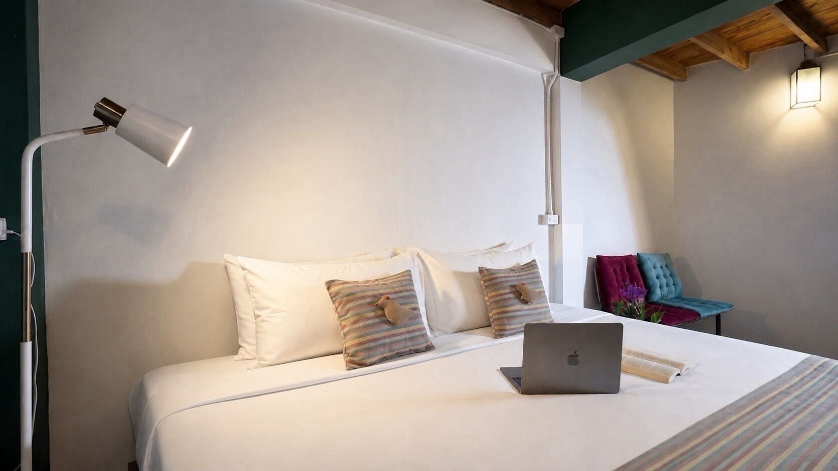A neatly made bed with pillows, a laptop, and a bedside lamp in a room with a simple, clean design.