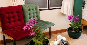 A room with a tufted green chair, a red cushioned chair, and a small table with a potted plant and a rolled-up white towel. - Retro at Mae Rim (Mae Rim)