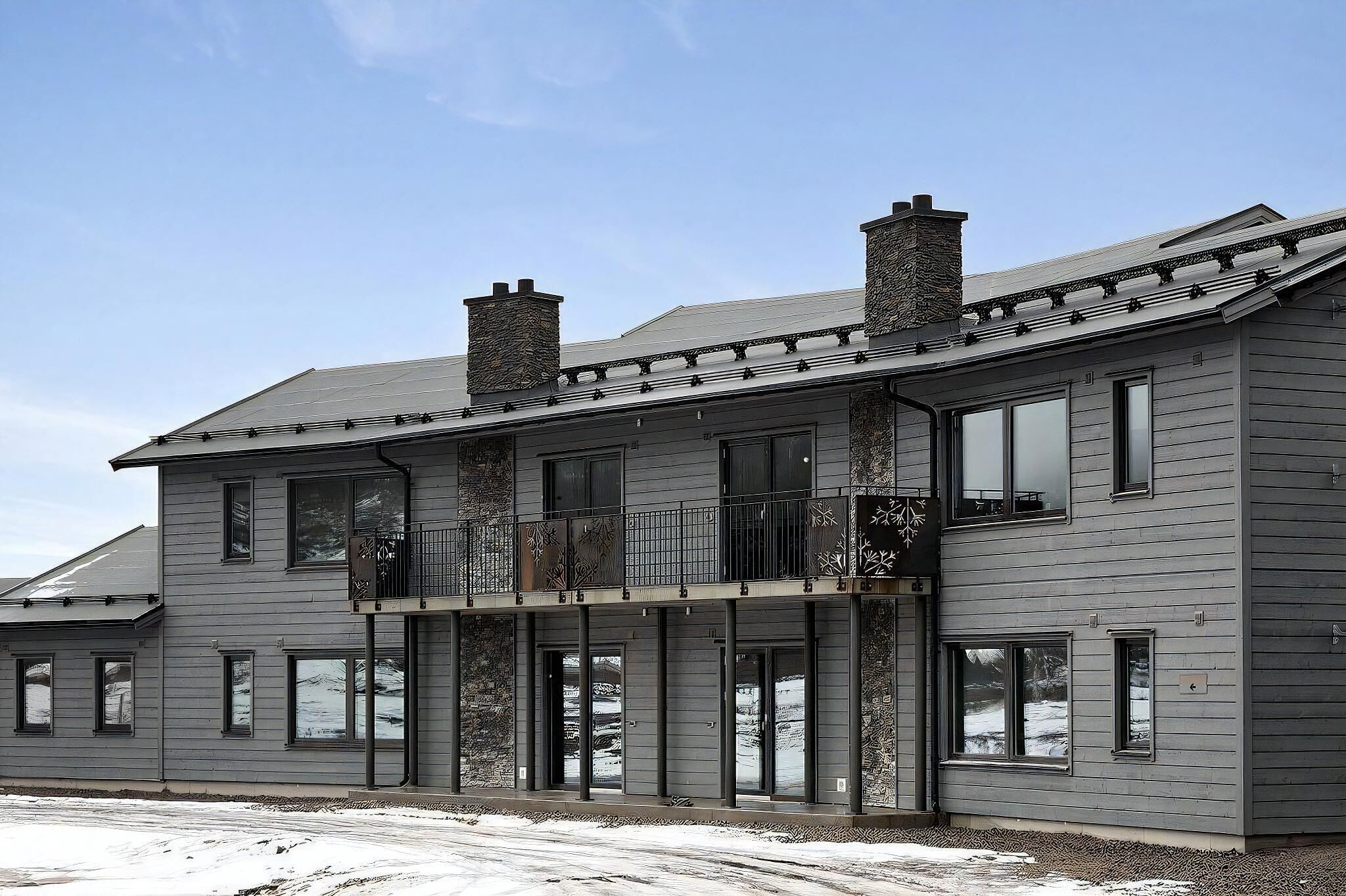 A two-story building with a balcony, large windows, and a stone chimney.
