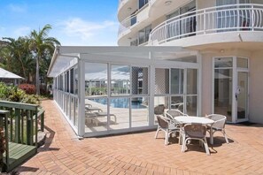A covered outdoor area with a pool, a table with chairs, and a view of a building with balconies. - Ocean View Coastal Haven in Burleigh Heads (Gold Coast)