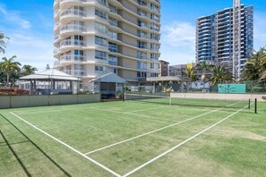 A tennis court with a net, surrounded by a fence, and buildings in the background. - Ocean View Coastal Haven in Burleigh Heads (Gold Coast)