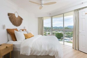 A bedroom with a bed, a ceiling fan, a large window, and a view of the outside. - Ocean View Coastal Haven in Burleigh Heads (Gold Coast)