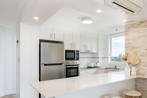 A modern kitchen with white cabinetry, stainless steel appliances, and a large island with seating. - Ocean View Coastal Haven in Burleigh Heads (Gold Coast)