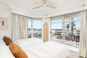 A bedroom with a bed, a ceiling fan, large windows, and a view of buildings. - Ocean View Coastal Haven in Burleigh Heads (Gold Coast)