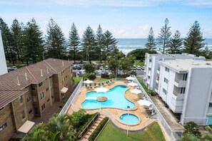 A pool area with a unique design, surrounded by apartment buildings, and overlooking a body of water. - Ocean View Coastal Haven in Burleigh Heads (Gold Coast)
