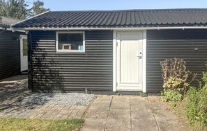 A single-story building with a dark exterior, a white door, and a small window. - 3 bedroom stunning home in Eskebjerg (Eskebjerg)
