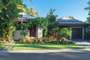 A modern house with a garage, surrounded by a well-maintained garden with various plants and a lawn. - Luxury 5-Bed Beachfront Mirage Villa with Pool (Port Douglas)
