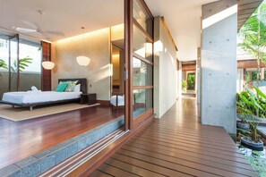 A modern bedroom with a bed, bedside table, and a view of a lush garden. - Luxury 5-Bed Beachfront Mirage Villa with Pool (Port Douglas)