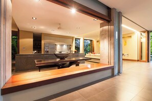 A modern kitchen with a central island, built-in appliances, and a dining area with a bench. - Luxury 5-Bed Beachfront Mirage Villa with Pool (Port Douglas)