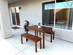 Un patio con una mesa y un banco de madera, una planta en maceta y un accesorio de luz fijado a la pared.