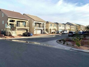 Una calle residencial con casas, un camino de entrada y coches estacionados.