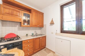 Une cuisine avec des meubles en bois, une cuisinière à gaz, un évier et une fenêtre donnant sur un paysage verdoyant.