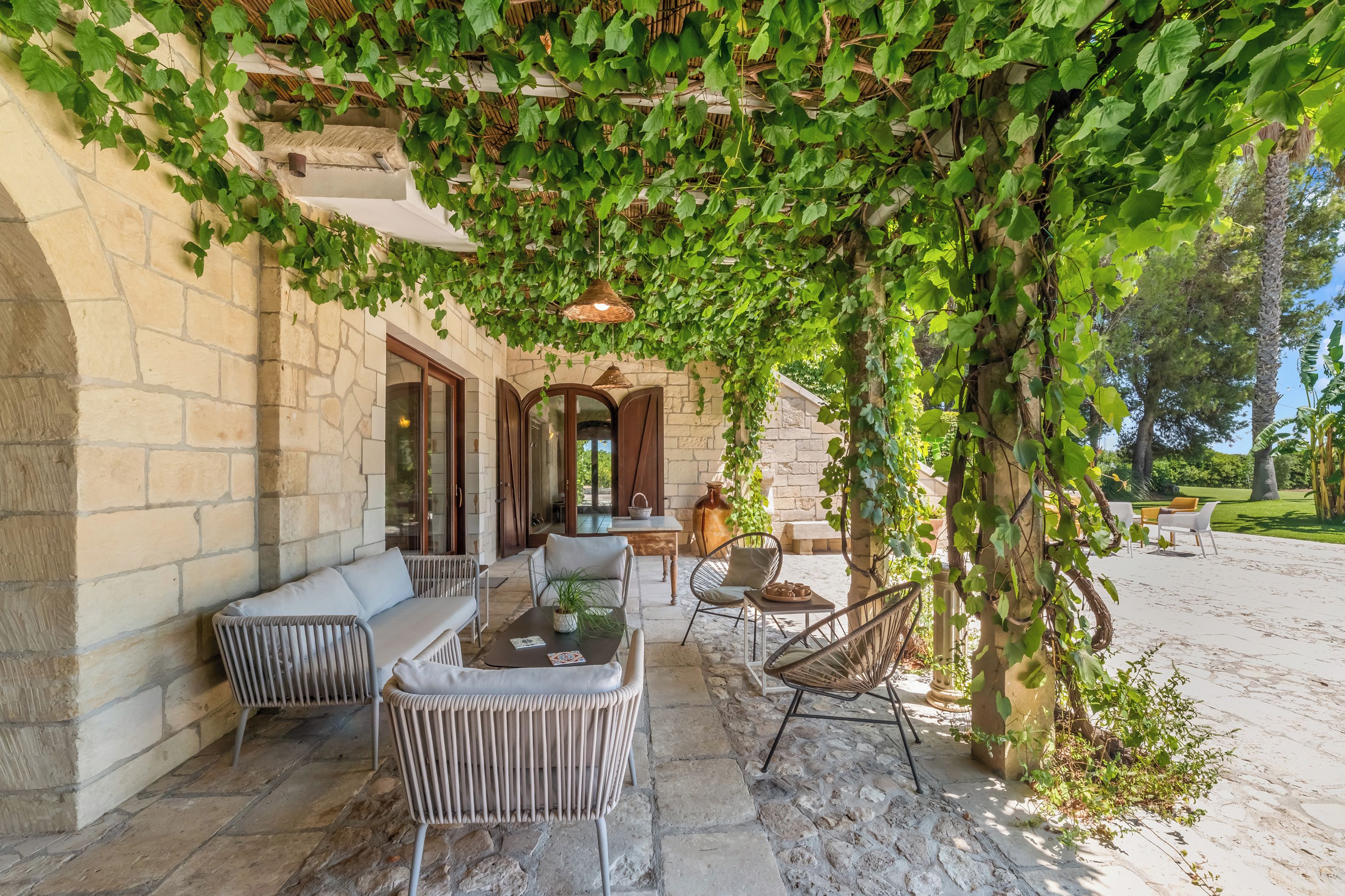 A covered outdoor seating area with stone walls, wicker furniture, and a hanging light fixture.