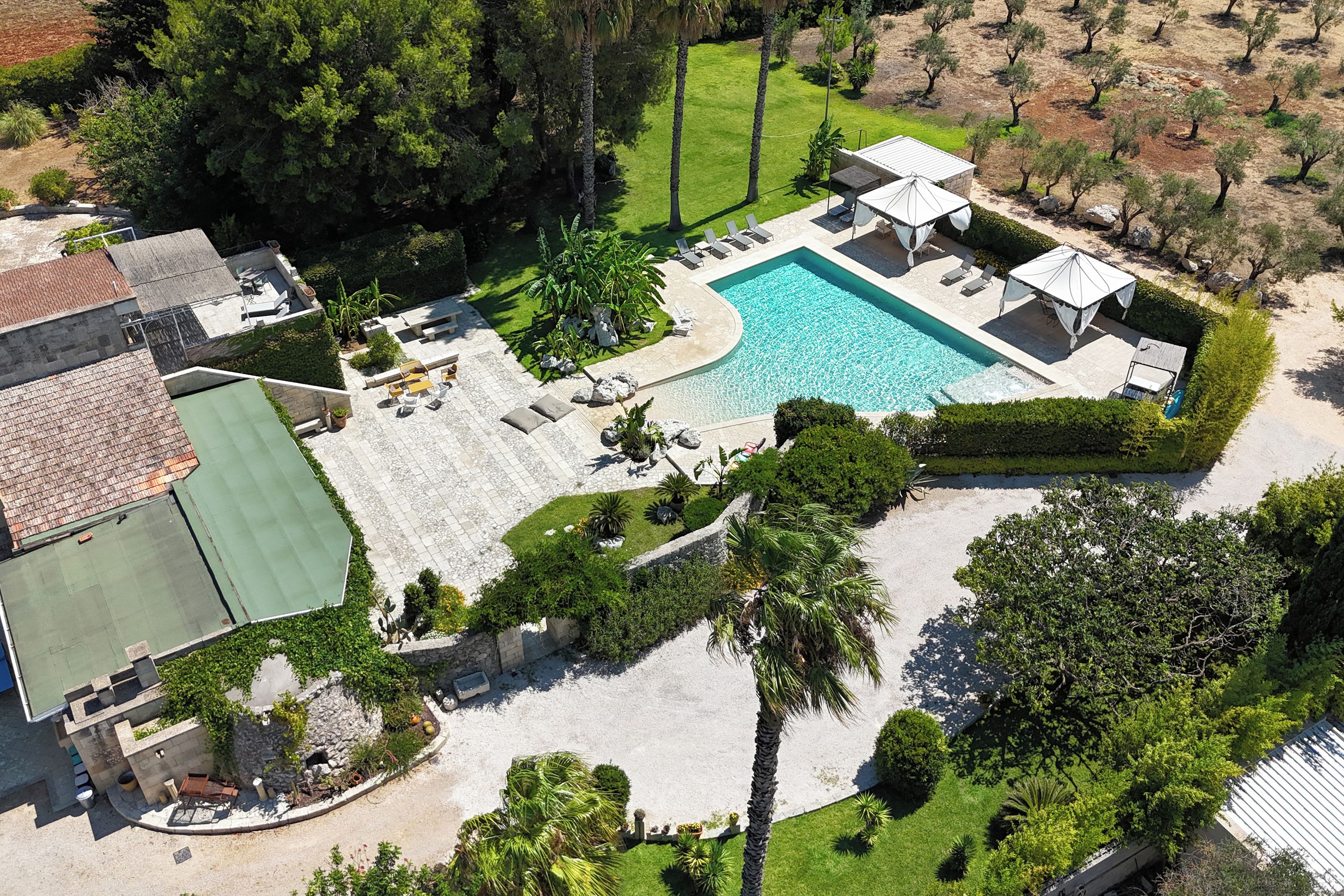 An aerial view of a property with a swimming pool, outdoor seating, and a tennis court.