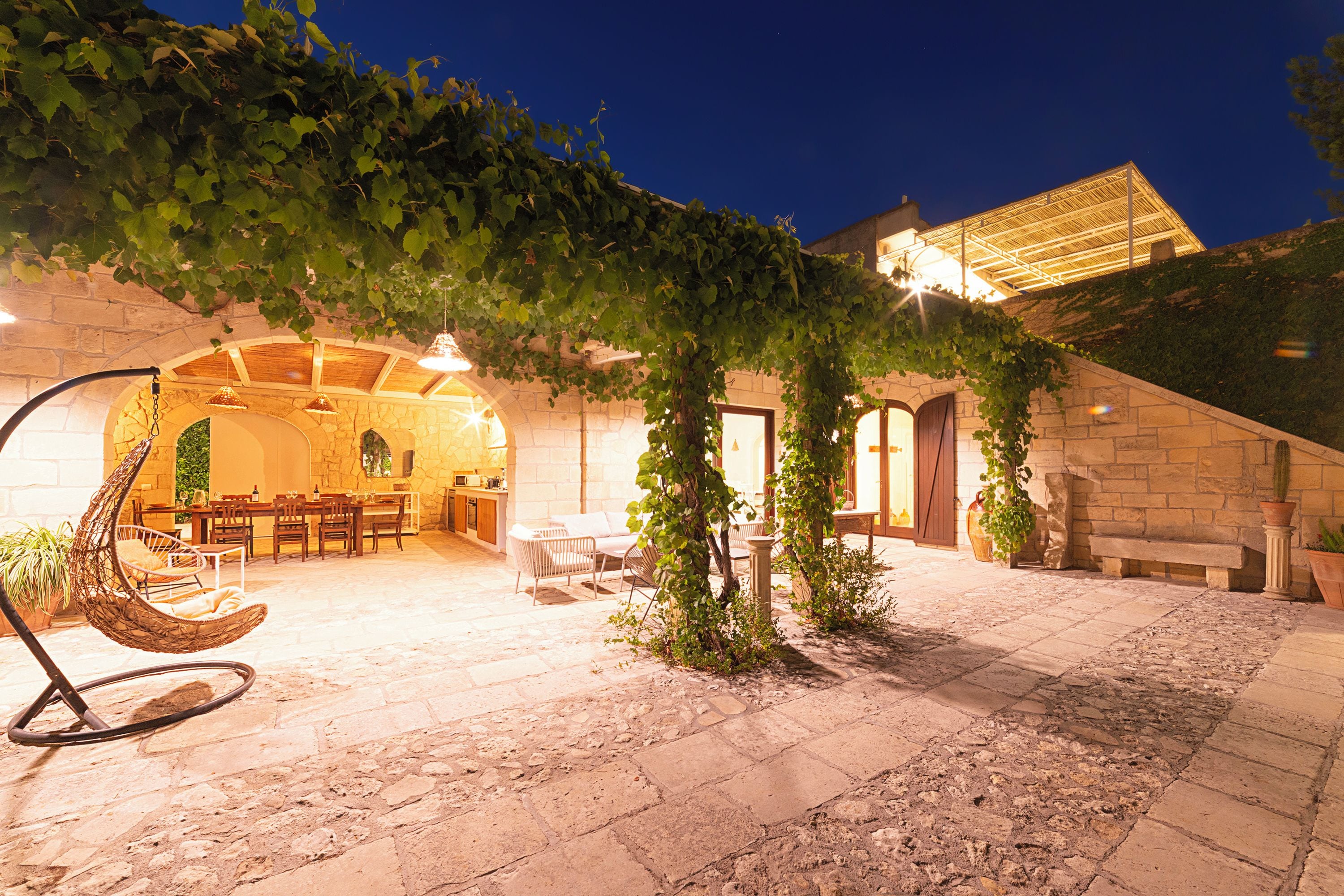 An outdoor patio with stone flooring, a hanging chair, and a dining area with tables and chairs.
