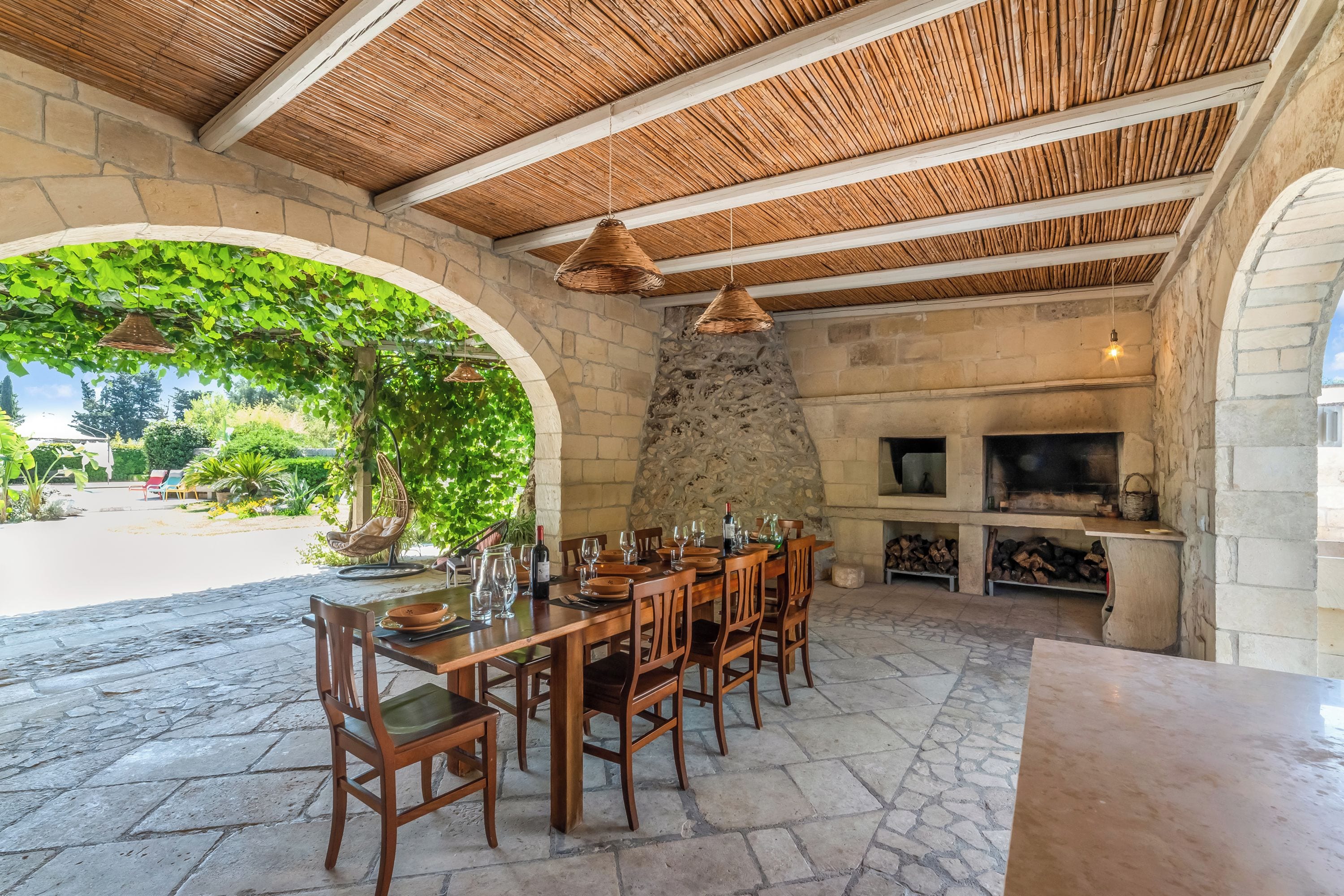An outdoor dining area with stone walls, wooden furniture, and a stone fireplace.