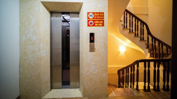 Een lift met een digitaal scherm, een bordje ‘niet roken’ en een bordje ‘geen brand’ op de muur.