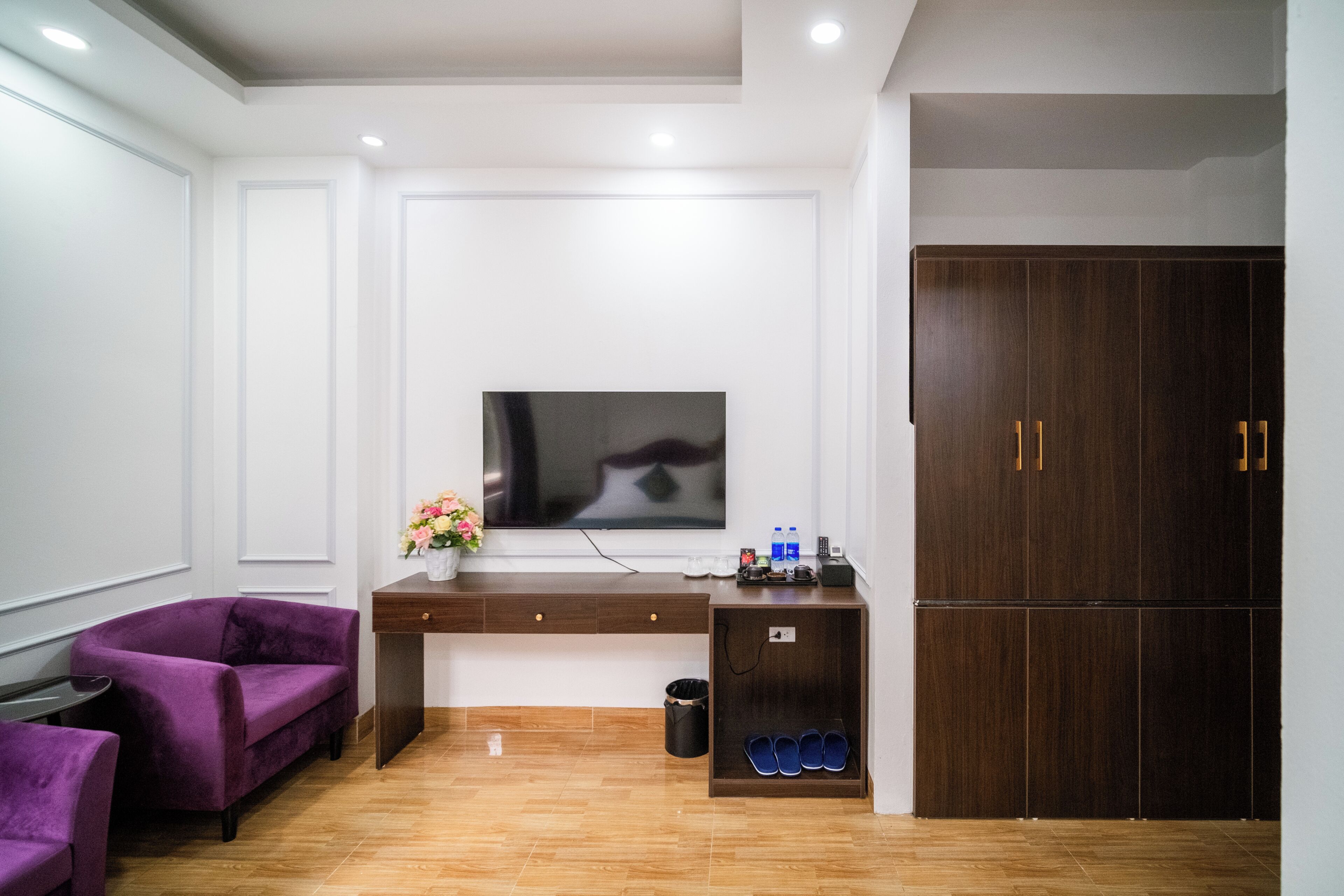Een moderne hotelkamer met een houten vloer, een paarse bank, een bureau met een flatscreen televisie en een kledingkast.