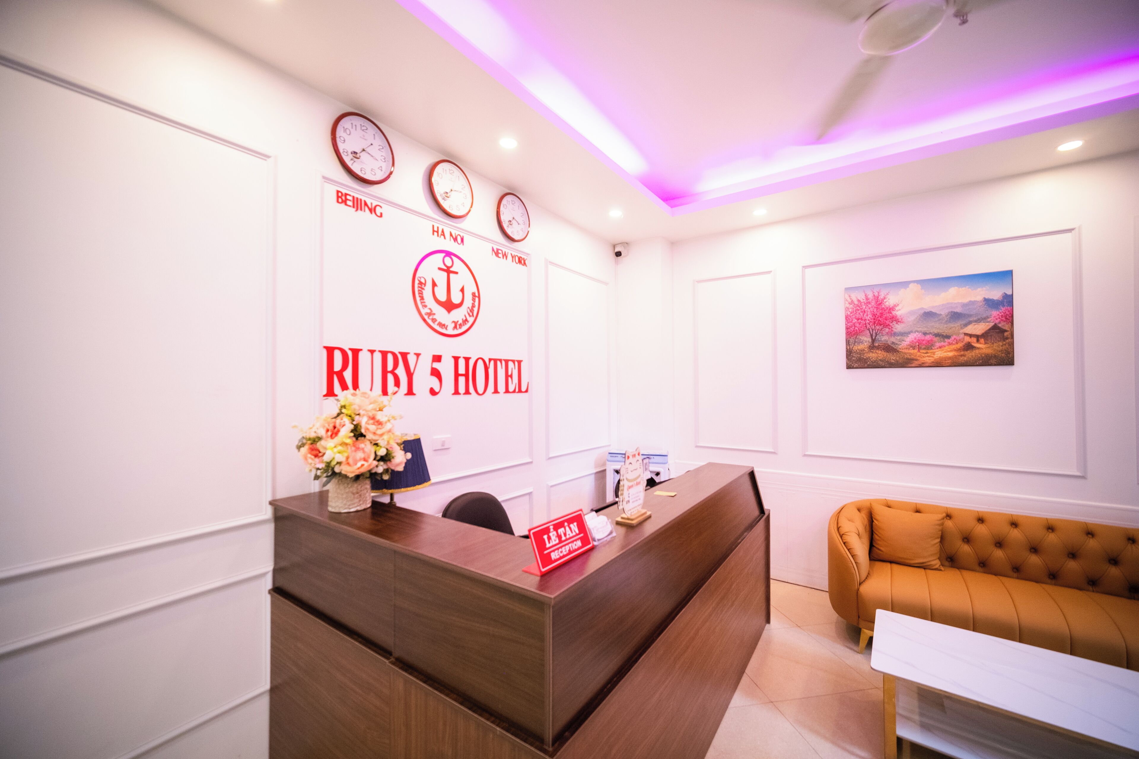 A hotel reception desk with clocks, a logo, and a painting on the wall.