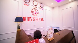 Een vergaderzaal met een grote tafel, stoelen, een klok en een muur met de aanduiding 'Ruby 5 Hotel'.