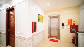 A hotel lobby with a wooden door, a wall-mounted elevator, and a welcome mat.
