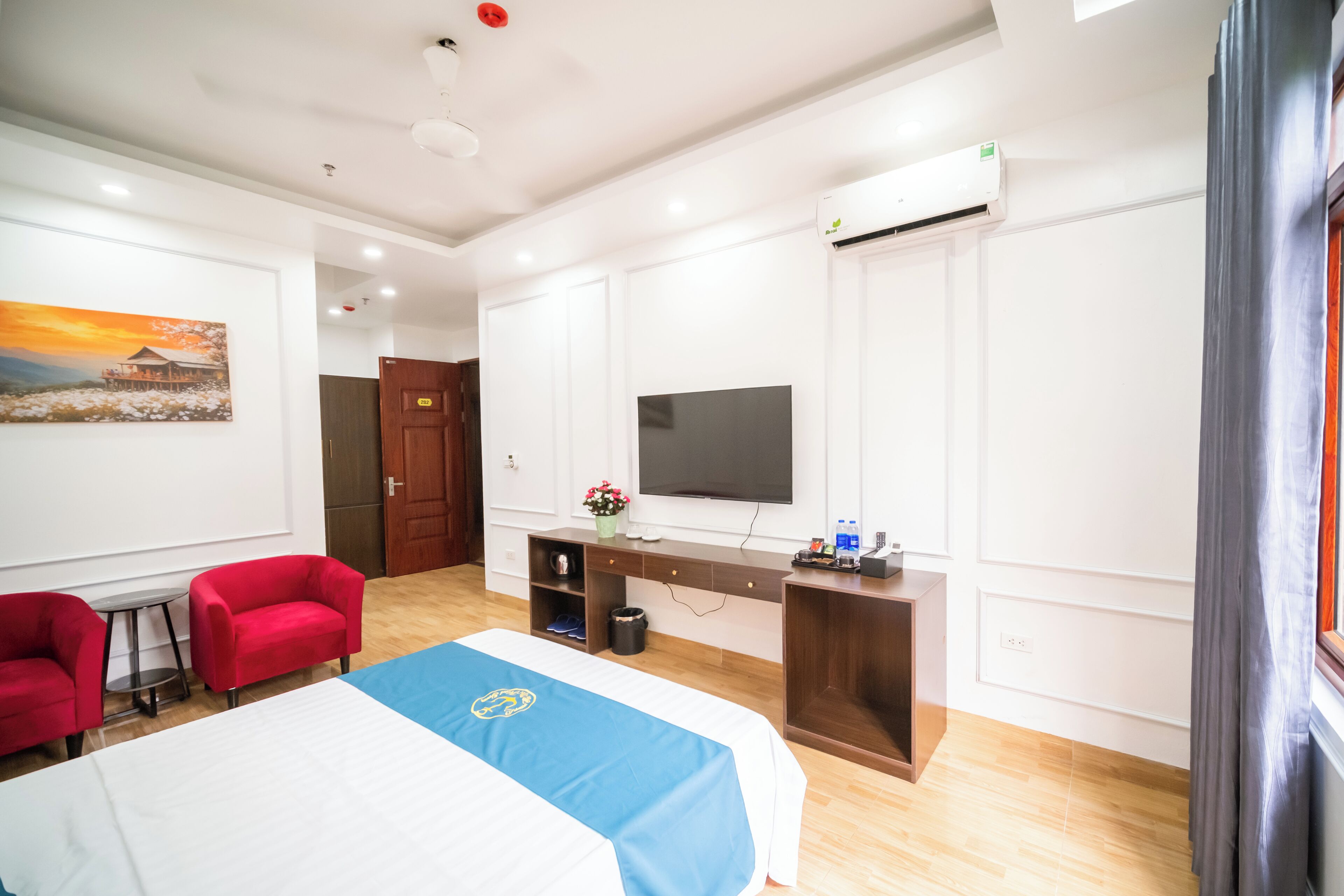 A hotel room with a bed, a desk, a television, and a red chair.