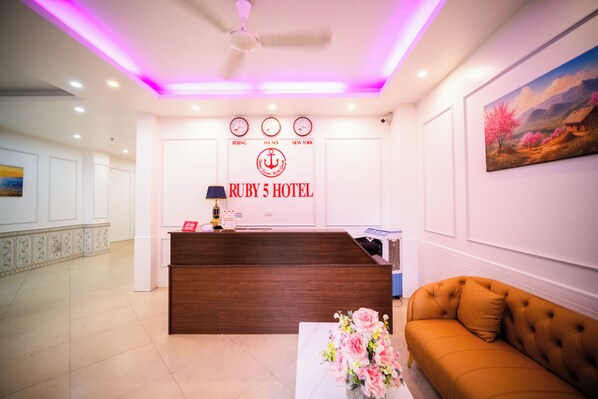 A hotel reception area with a wooden reception desk, a clock above it, and a painting on the wall. - RUBY 5 HOTEL (Yen Hoa)