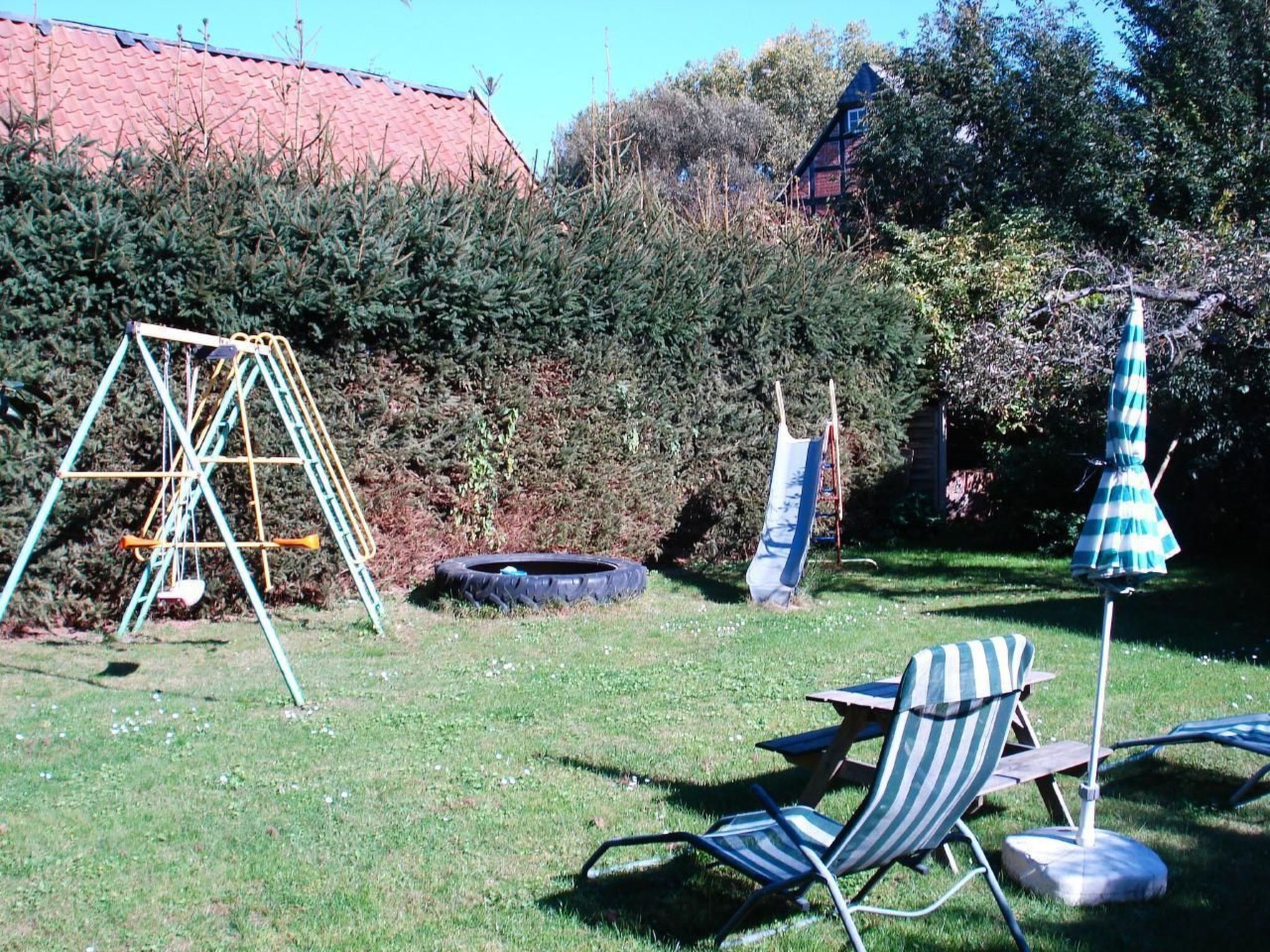 Une cour arrière avec une balançoire, une balançoire faite d’un pneu, une chaise de jardin à rayures et un parasol bleu.