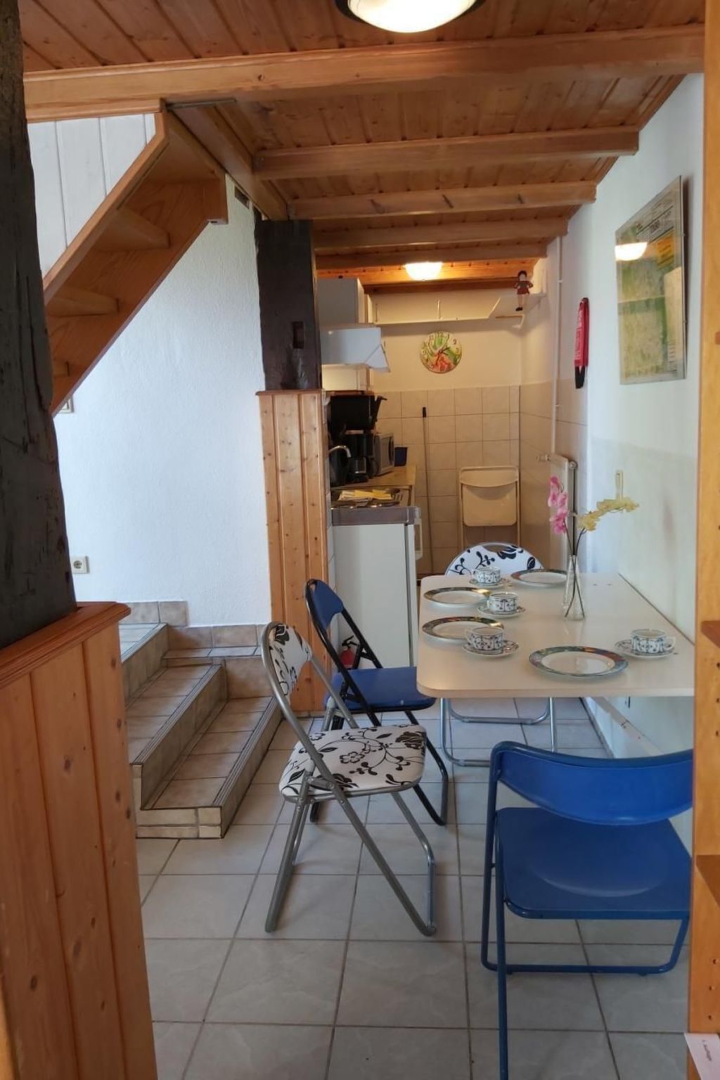 A dining area with a table set for two, chairs, and a kitchen in the background.
