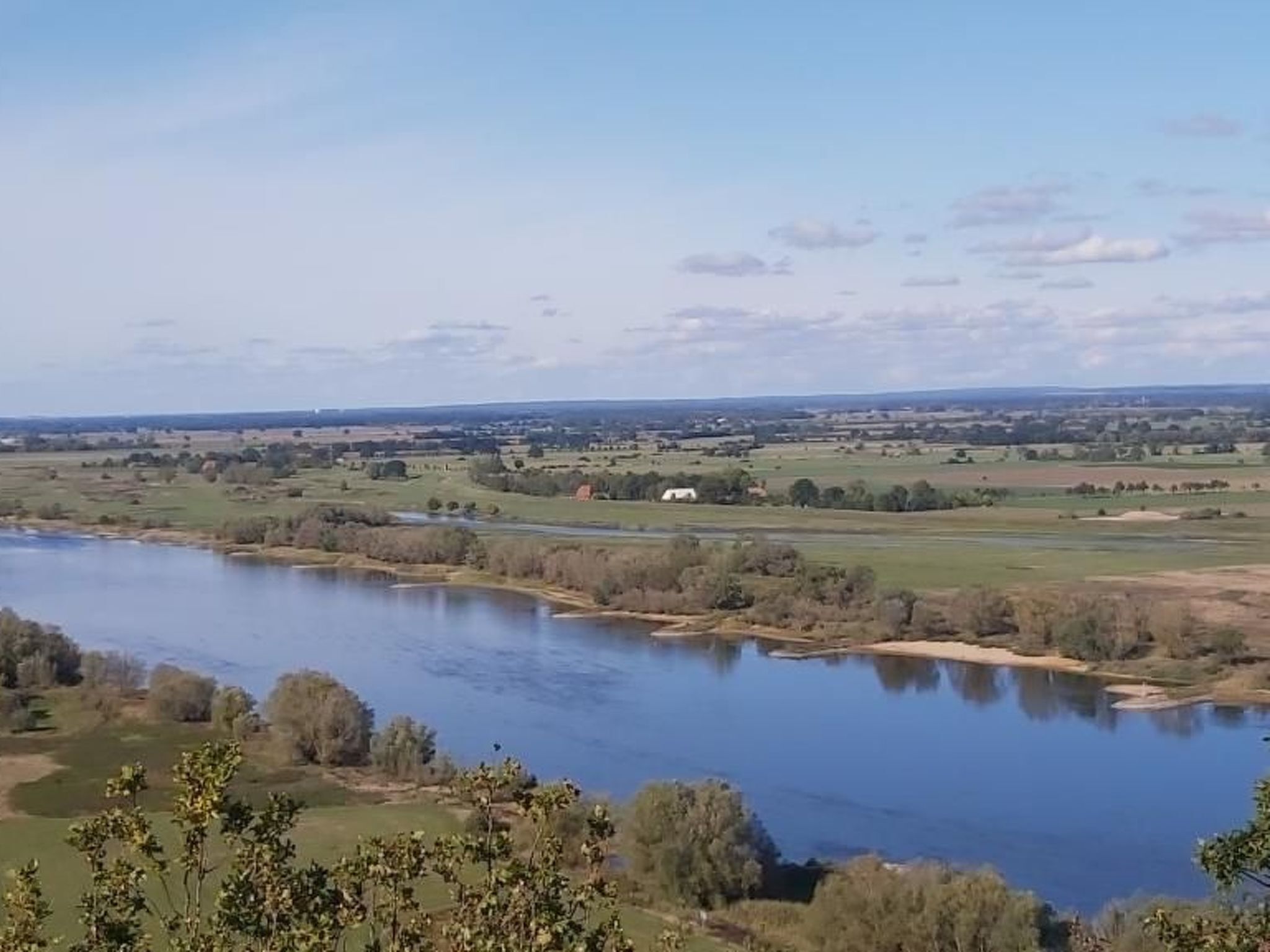 A river with a view of the countryside, including fields and a few buildings.