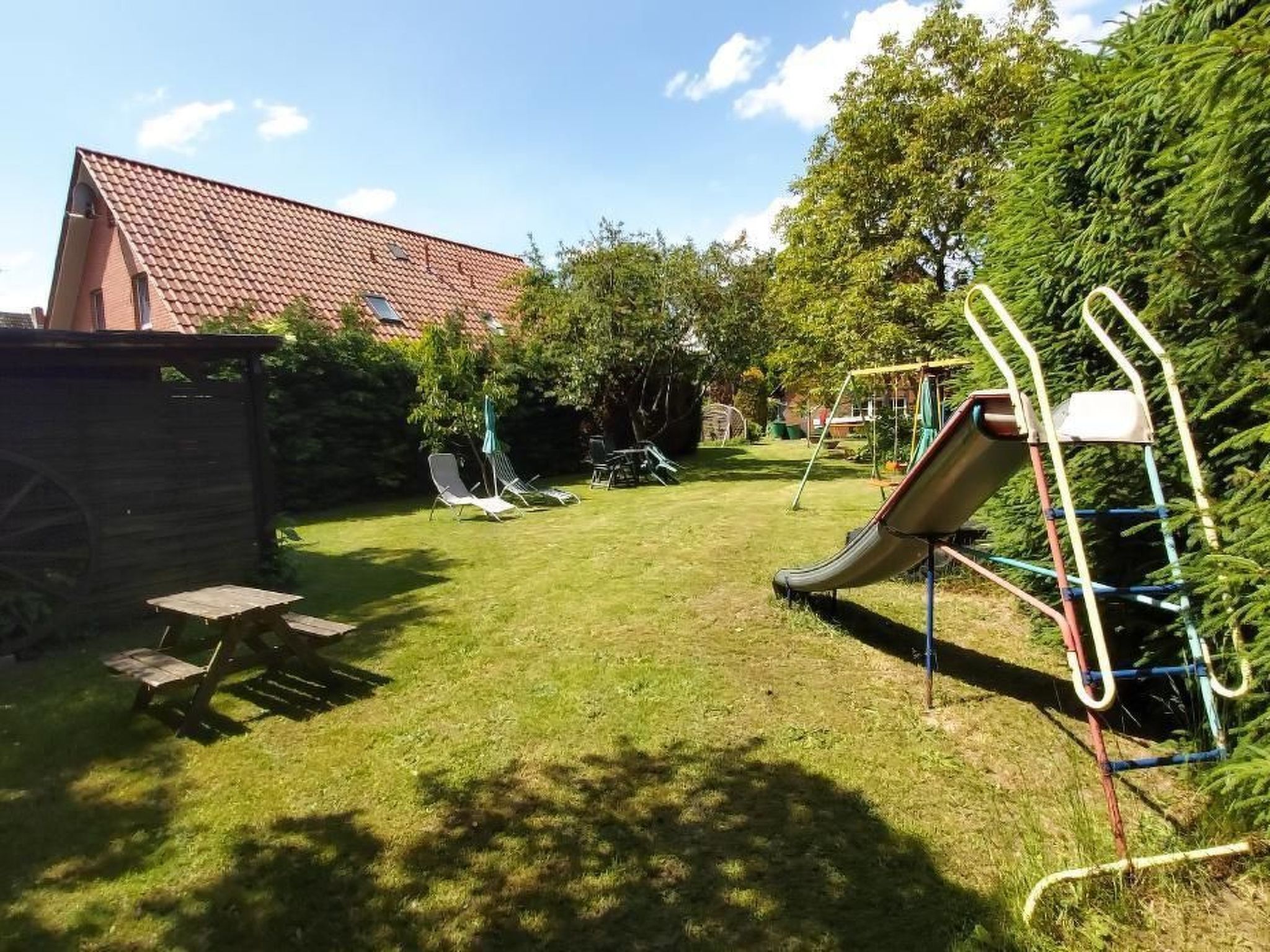 A backyard with a slide, a picnic table, and a fenced area.