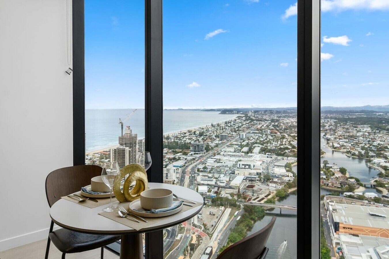 A dining area with a table set for two, overlooking a coastal cityscape with buildings and a river.
