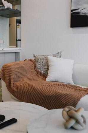 Un salon moderne avec un canapé recouvert d’une couverture tricotée marron, un coussin blanc et un coussin à motifs.