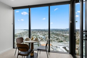 A modern room with a panoramic city view through large windows, a round table with chairs, and a small decorative vase. - Luxury 1BR with Stunning Ocean Views (Broadbeach)