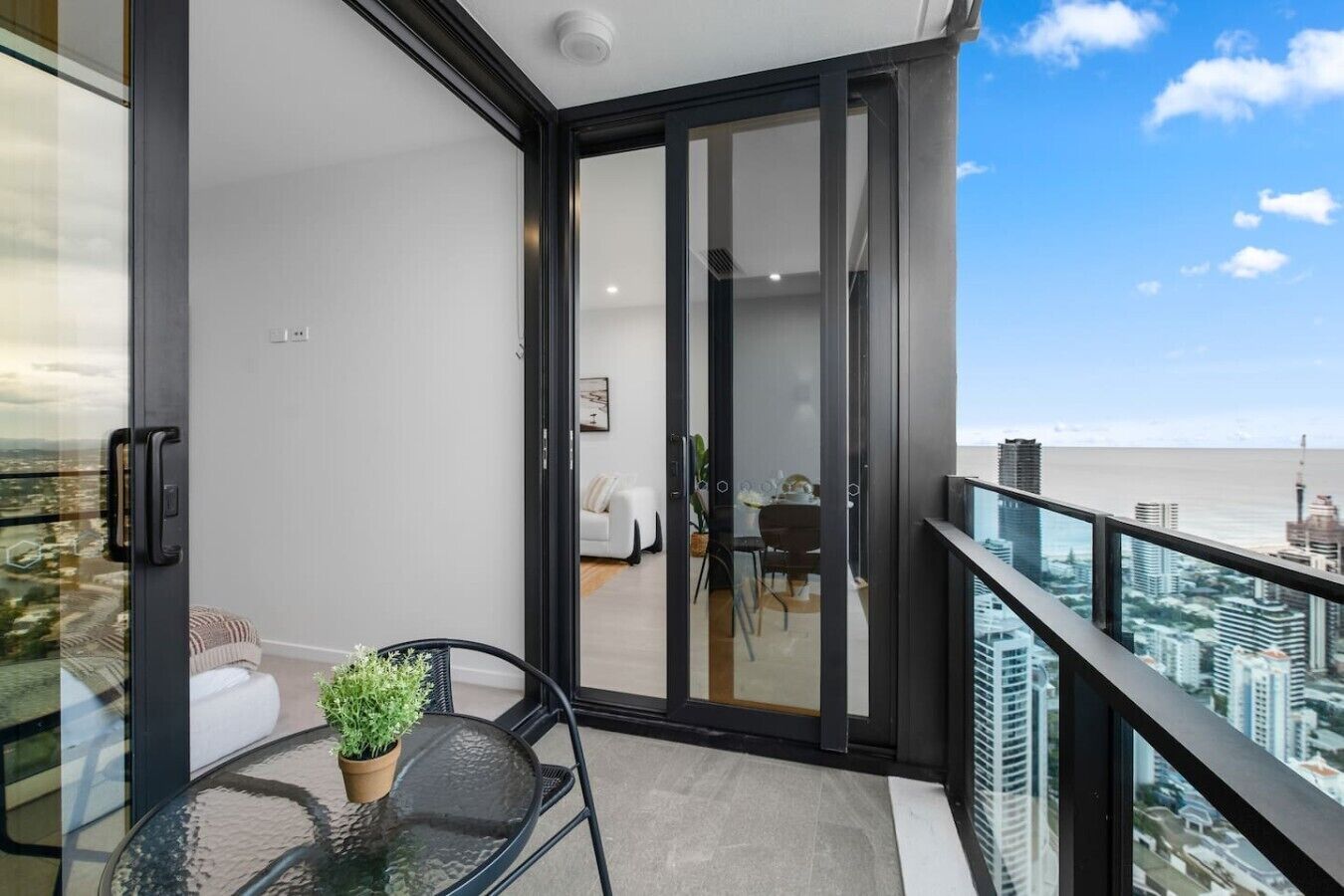 A balcony with a glass door leading to a living area, a dining table with chairs, and a potted plant.