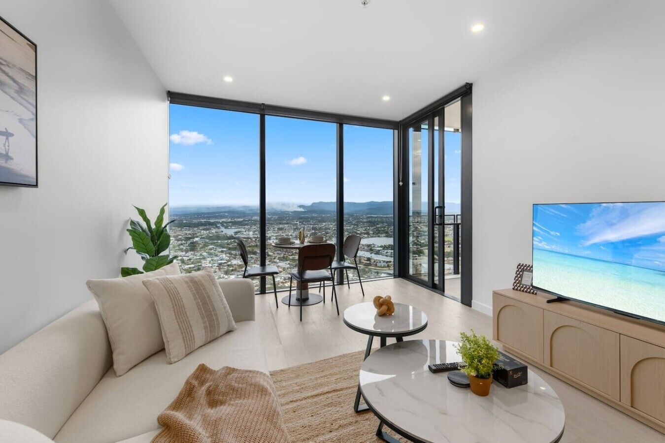 Ein modernes Wohnzimmer mit großem Fernseher, einer Couch, einem Couchtisch und einem Balkon mit Blick auf die Stadt.