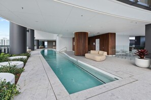 A modern indoor pool area with a long pool, seating, and a glass railing. - Luxury 1BR with Stunning Ocean Views (Broadbeach)