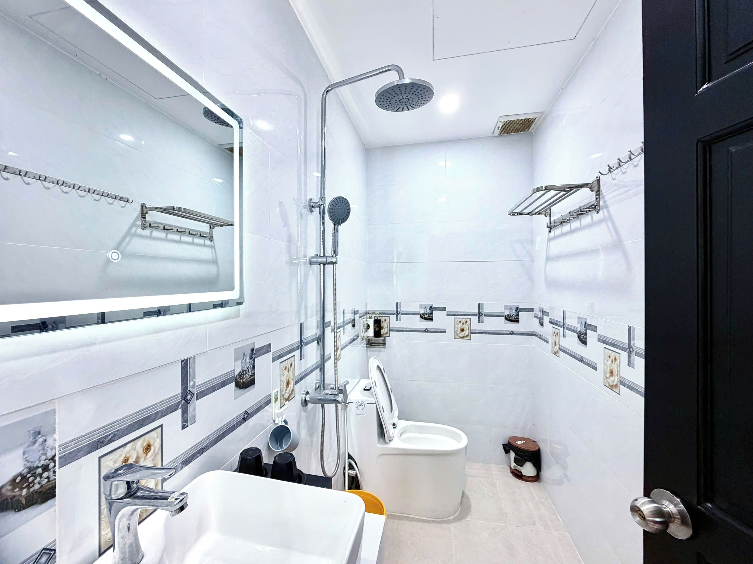 A modern bathroom with a large mirror, a shower, a toilet, and a sink.