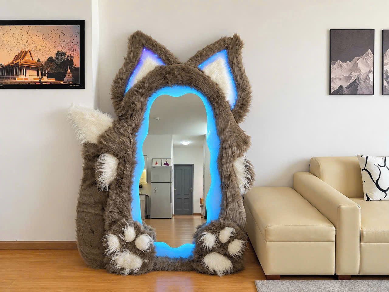 A room with a large mirror shaped like a cat's head, a beige sofa, and a framed picture on the wall.