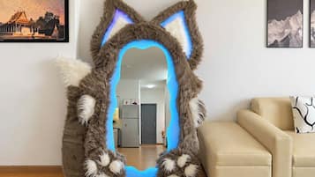 A room with a large mirror shaped like a cat's head, a beige sofa, and a framed picture on the wall.