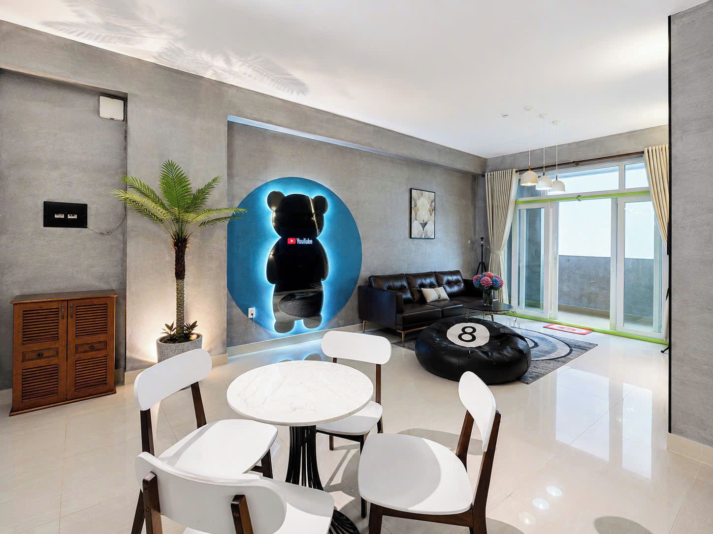 A modern living room with a glass door leading to a balcony, a black sofa, a coffee table with a number, and a potted plant.