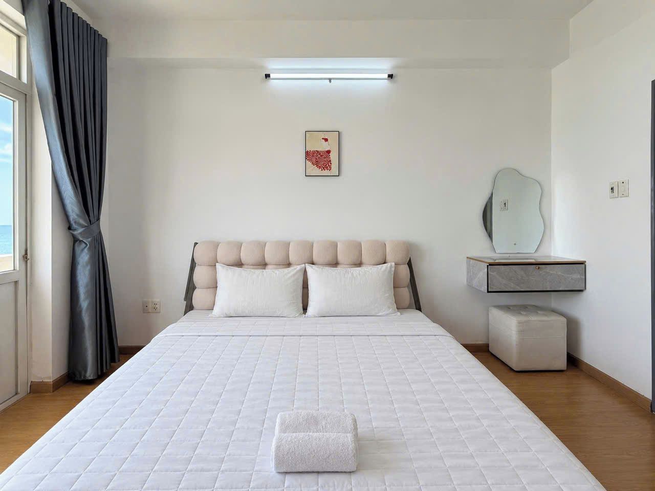 Un dormitorio con una cama grande, una mesita de noche, un espejo y una ventana con cortinas.