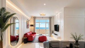 A modern living room with a red sofa, a glass dining table, and a view of the sea through large windows. - MOC AN COLLECTION-Blue Sea Beachfront VT (Vung Tau)
