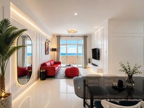 A modern living room with a red sofa, a glass dining table, and a view of the sea through large windows. - MOC AN COLLECTION-Blue Sea Beachfront VT (Vung Tau)