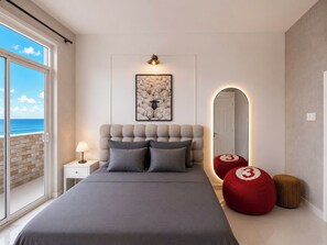 A bedroom with a large bed, a nightstand, a lamp, a framed picture, a mirror, and a view of the ocean. - MOC AN COLLECTION-Blue Sea Beachfront VT (Vung Tau)