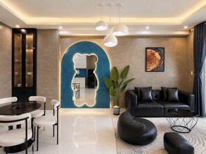 A modern living room with a black leather sofa, a dining table with chairs, a coffee table, and a large potted plant. - MOC AN COLLECTION-Blue Sea Beachfront VT (Vung Tau)
