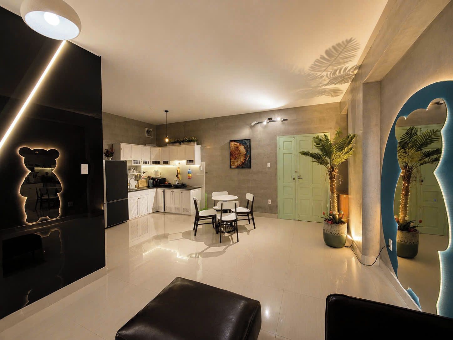 Una cocina moderna con armarios blancos, una zona de comedor con mesa y sillas blancas, y un espacio de sala con un espejo grande y una puerta verde.